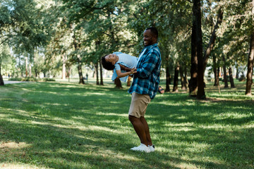 Fototapeta premium happy african american father holding in arms cute son in park