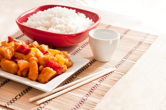 Sweet and sour chicken with bell pepper and pineapple. White rice on background