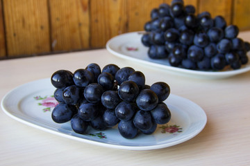 Bunches of fresh ripe red grapes on a white plate on a wooden light background. Grapes background. Sweet, juicy, ripe grape. Harvest of organic local grapes. Healthy food with vitamins.