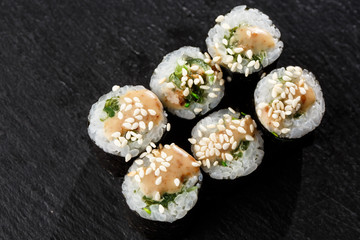 Maki Sushi Rolls with wakame and nut sauce on black stone on dark background. Sushi menu. Japanese food. Closeup of delicious japanese food with sushi roll. Horizontal photo