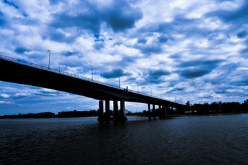Fototapeta na wymiar large road bridge over the river, contrasting clouds and blue sky, dramatic