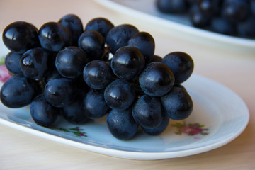 Bunches of fresh ripe red grapes on a white plate on a wooden light background. Grapes background. Sweet, juicy, ripe grape. Harvest of organic local grapes. Healthy food with vitamins.