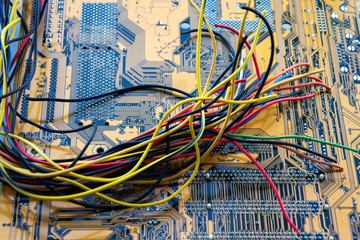 The bunch of electric wires of different colors are very much intertwined on the background of the motherboard PCB.
