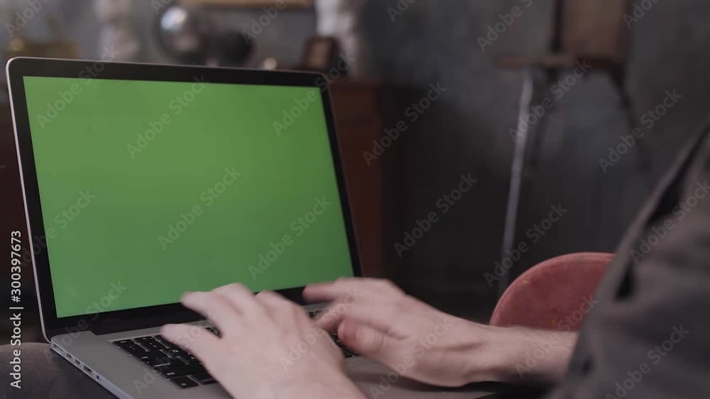 Poster over the shoulder view of a man sitting at his desk and working on a laptop with green screen. stock