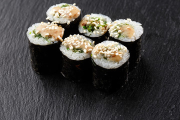 Maki Sushi Rolls with wakame and nut sauce on black stone on dark background. Sushi menu. Japanese food. Closeup of delicious japanese food with sushi roll. Horizontal photo