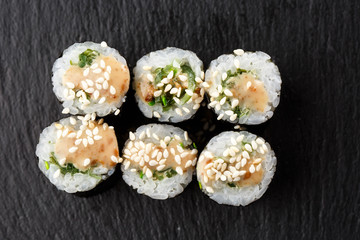 Maki Sushi Rolls with wakame and nut sauce on black stone on dark background. Sushi menu. Japanese food. Closeup of delicious japanese food with sushi roll. Horizontal photo