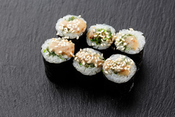 Maki Sushi Rolls with wakame and nut sauce on black stone on dark background. Sushi menu. Japanese food. Closeup of delicious japanese food with sushi roll. Horizontal photo