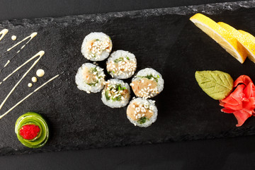 Maki Sushi Rolls with wakame and nut sauce on black stone on dark background. Sushi menu. Japanese food. Closeup of delicious japanese food with sushi roll. Horizontal photo