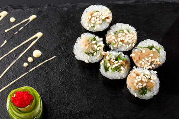 Maki Sushi Rolls with wakame and nut sauce on black stone on dark background. Sushi menu. Japanese food. Closeup of delicious japanese food with sushi roll. Horizontal photo