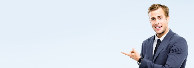 Smiling businessman pointing at something, over grey background. Copy space for some slogan or...