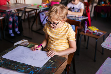 Fototapeta premium Blonde boy with glasses drawing. Group of elementary school pupils in classroom on art class. Russia, Krasnodar, May, 23, 2019