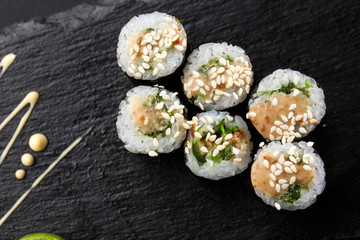Maki Sushi Rolls with wakame and nut sauce on black stone on dark background. Sushi menu. Japanese food. Closeup of delicious japanese food with sushi roll. Horizontal photo