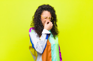 young pretty woman feeling disgusted, holding nose to avoid smelling a foul and unpleasant stench...