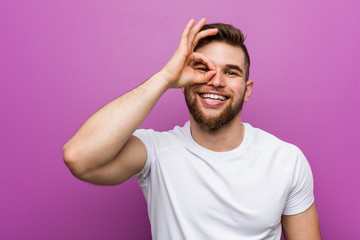 Young handsome caucasian man excited keeping ok gesture on eye.