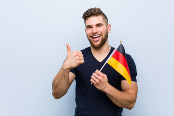 Young caucasian man holding a germany flag smiling and raising thumb up