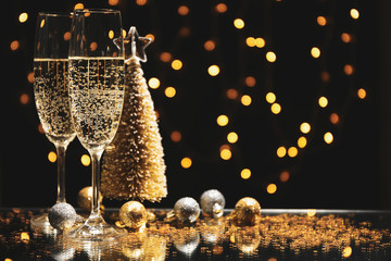 Champagne glasses and baubles against blurred lights background, space for text