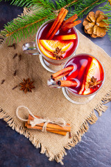 Red mulled wine and fir branches on burlap. Mulled wine with oranges, honey, cinnamon and cloves on a dark background. Hot wine with honey and spices