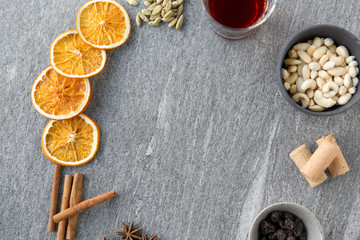 christmas and seasonal drinks concept - hot mulled wine, dry orange slices, raisins with cashew nuts and aromatic spices on grey background