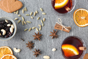 christmas and seasonal drinks concept - hot mulled wine, dry orange slices, raisins with cashew nuts and aromatic spices on grey background