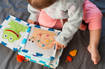 Baby girl playing with her textile book. Page with felt frog and snail. Woolly toys. Baby development. Educational toys. Fine motor skills. Little colorful buttons.