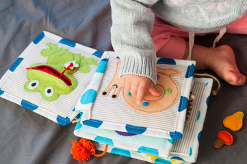 Baby girl playing with her textile book. Page with felt frog and snail. Woolly toys. Baby...