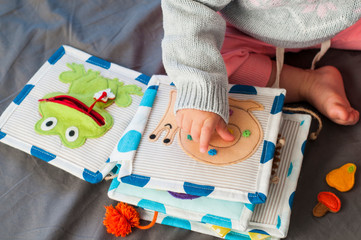 Baby girl playing with her textile book. Page with felt frog and snail. Woolly toys. Baby development. Educational toys. Fine motor skills. Little colorful buttons.