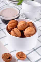 Walnut shaped cookies with condensed milk in a round box and a cup of coffee