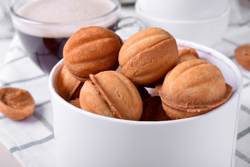 Walnut shaped cookies with condensed milk in a round box and a cup of coffee