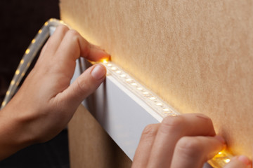 the master glues the LED strip into the niche of the shelf from the cabinet for lighting.installation of diode lighting tape