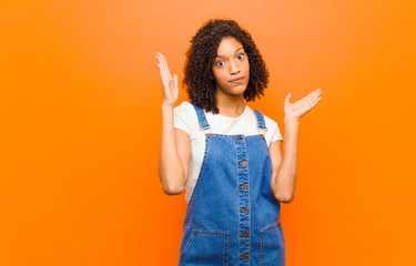 young pretty black woman looking shocked and astonished, with jaw dropped in surprise when...