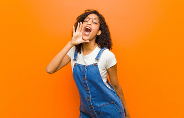 young pretty black woman yelling loudly and angrily to copy space on the side, with hand next to...