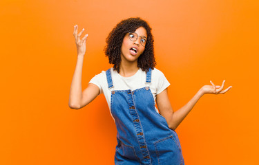 young pretty black woman shrugging with a dumb, crazy, confused, puzzled expression, feeling...