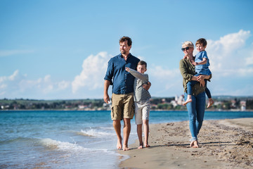 Young family with two small children walking outdoors on beach.