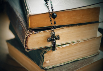Old battered thick books on magic and rituals and a black Gothic cross on a chain.