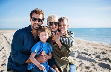 Young family with two small children sitting outdoors on beach.