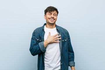 Young hispanic cool man laughs out loudly keeping hand on chest.