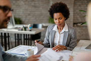 African American insurance agent analyzing her client's financial reports in the office.