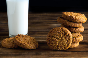 Group of oatmill cookies and milk glass on wooden surface - close up