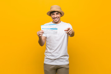 Young hispanic man holding an air tickets cheerful smiles pointing to front.