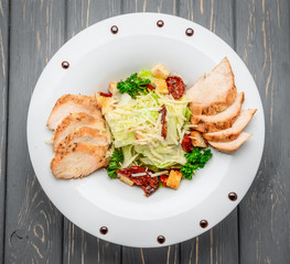 Caesar salad with croutons, quail eggs, cherry tomatoes and grilled chicken on a wooden background