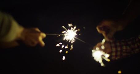 Close up, people hold sparklers at night