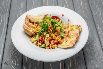 Caesar salad with croutons, quail eggs, cherry tomatoes and grilled chicken on a wooden background