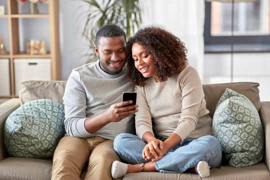 technology, internet and people concept - happy african american couple with smartphone at home