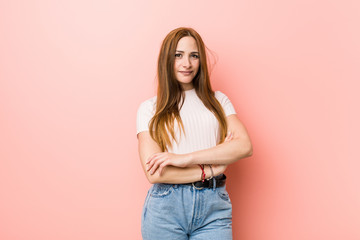 Young redhead ginger woman against a pink wall who feels confident, crossing arms with determination.