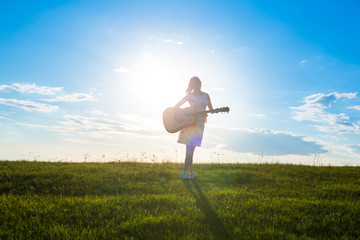 woman in dress holding the guitar on cloudy sunset sky