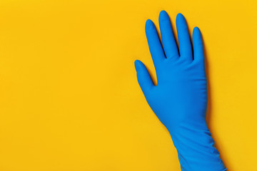 Hand in a protective blue glove on a yellow colored background