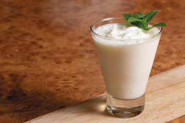 Kefir in a glass goblet with a mint branch on a wooden board on a brown background