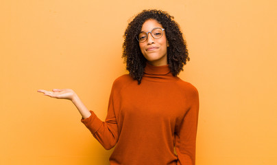 young pretty black woman feeling happy and smiling casually, looking to an object or concept held...