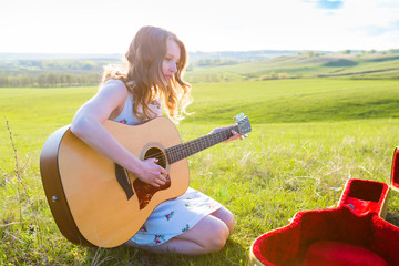 Beautiful young girl playing guitar in the field.