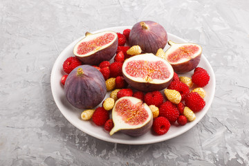 Fresh figs, strawberries and raspberries on white plate on gray concrete background. side view